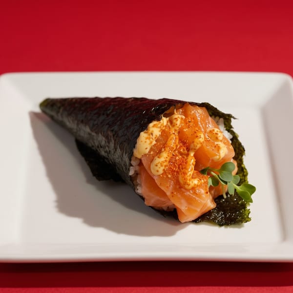 Salmon temaki hand roll with spicy mayo and microgreens on a white plate against a red background.