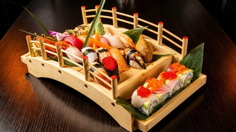 Assorted sushi and sashimi arranged on a wooden boat platter on a dark table.