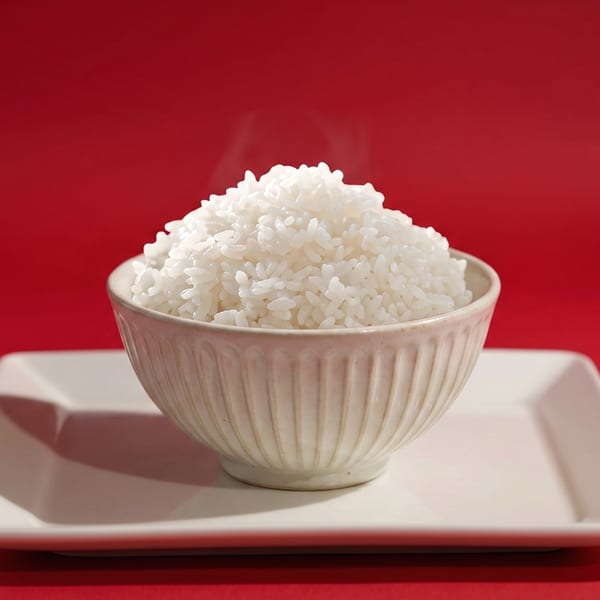 Steaming white rice piled high in a textured bowl, centered on a white rectangular plate against a red background.